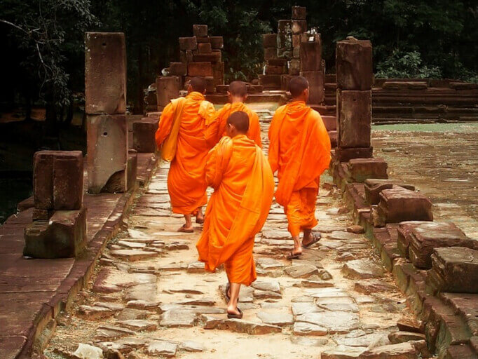 Thailändische Buddhisten gehen in ihren orangen Gewändern einen Weg entlang